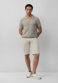 Una camiseta polo de manga corta a rayas de color marrón claro se combina con unos pantalones cortos crema hasta la rodilla. Las zapatillas son de color beige con detalles oscuros y cordones.