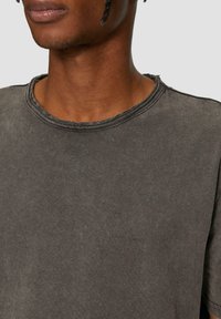 Czarnoszary t-shirt z krótkim rękawem i okrągłym dekoltem, z wyraźnym efektem wyblaknięcia i surowymi brzegami. Prosty design z minimalnymi detalami.