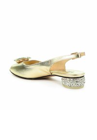 Złote metaliczne buty slingback z okrągłym noskiem, wyposażone w okrągły akcent na cholewce oraz niskim obcasem zdobionym kryształami.