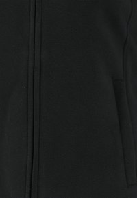 Sort fleecejakke med en glat tekstur, der har en frontlynlås og sidelommer. Enkel design uden synlige mønstre eller udsmykninger.