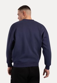 Felpa blu navy con collo rotondo, spalle scese e polsini a costine. Il tessuto appare liscio con dettagli di cucitura minimi.