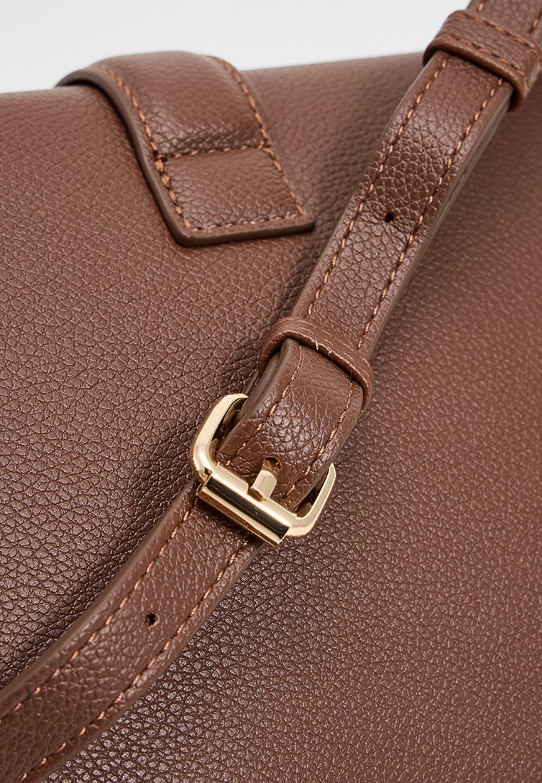 Bolso de cuero marrón texturizado con un cierre de hardware dorado en una correa, que presenta un acabado suave y un detalle de costura visible.
