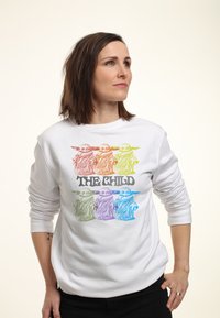 Vit sweatshirt med en flerfärgad grafisk bild av en karaktär med stora öron, med titeln "THE CHILD" i fet svart text nedan.