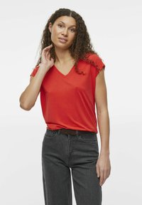 Camiseta roja de manga corta con cuello en V, confeccionada en una tela suave, combinada con jeans oscuros de cintura alta, que presentan un diseño sencillo y una textura sutil.