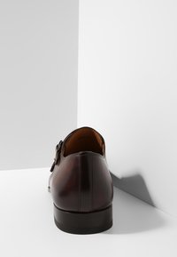 Chaussure en cuir marron avec un bout arrondi et un design élégant. Dispose d'un talon léger et d'un accent de boucle sur le côté. Texture lisse, finition polie.