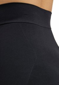Leggings neri a vita alta con un design a coste testurizzato; tessuto liscio con una forma aderente e dettagli cuciti lungo i lati.