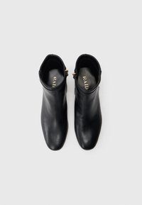 Botas de tornozelo em couro preto com um design elegante, bico fino e fechos de correr laterais. Apresentam uma textura suave e um brilho sutil. Logotipo da marca no interior.