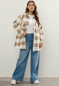 Ruudullinen paita vaaleassa kermassa ja ruskeassa, kahdella rintataskulla, yhdistettynä vaaleansinisiin leveälahkeisiin farkkuihin ja valkoisiin tennareihin. Rentoa, väljää muotoilua.