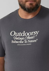 Grijze katoenen t-shirt met een ronde hals en korte mouwen. Witte tekst bevat "Outdoorsy," "Feelings Ahead," en "Subscribe To Nature."