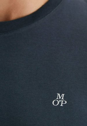 Nahaufnahme eines dunkelblauen Rundhalsausschnitt-Shirts mit weißen Buchstaben "M O'P" auf dem oberen Brustbereich gedruckt.