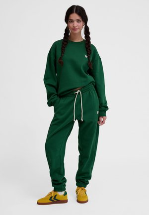 Groene sweatshirt en bijpassende joggers van zachte stof, voorzien van een klein logo, een trekkoord in de taille en ribgebreide manchetten. Gecombineerd met gele sneakers.
