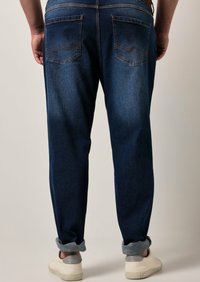 Tumma siniset denim-farkut suoralinjaisella mallilla, joissa on viisi taskua, ommellut takataskut yksityiskohtina ja käännetyt lahkeet. Yhdistetty vaaleisiin kenkiin.