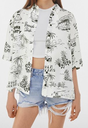 Short-sleeve, white shirt with black tropical-themed prints, including palm trees and skulls, paired with frayed denim shorts.