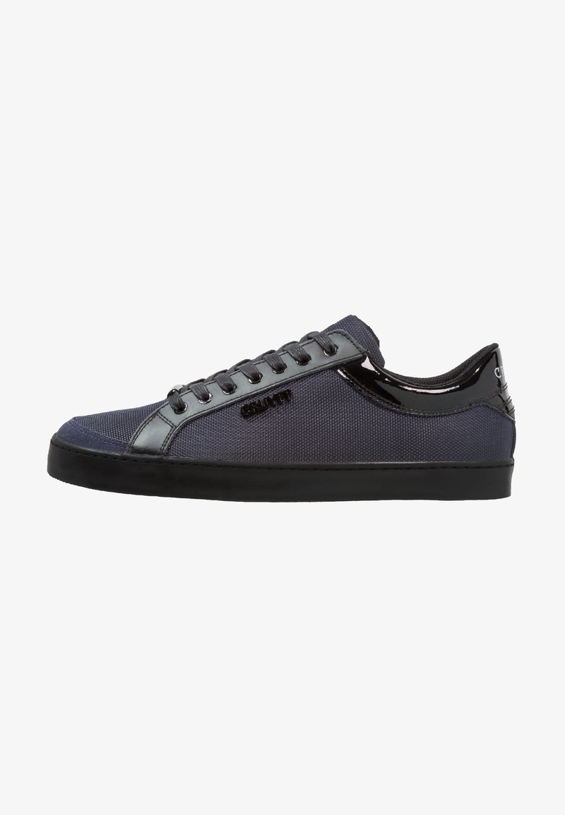 Baskets basses bleu foncé avec lacets noirs, semelle noire, et détails brillants noirs au talon et sur les bordures.