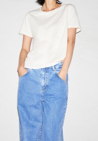Weißes Baumwoll-T-Shirt mit kurzen Ärmeln, kombiniert mit hellblauen Jeanshosen mit Fronttaschen und geradem Bein-Design.