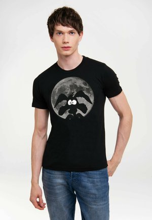 Camiseta de algodón negra con un gráfico circular de un personaje de estilo caricatura frente a una luna llena, con ojos distintivos y orejas prominentes.