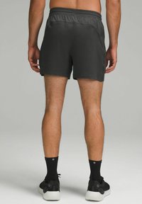 Shorts de sport pour hommes en gris foncé avec une taille élastique, texture lisse et un design minimaliste, portés avec des chaussettes et des chaussures noires.