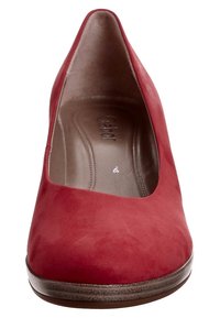 Scarpa con tacco alto in suede rosso, con punta arrotondata, texture liscia e tacco basso a strati. L'interno presenta il logo impresso sulla soletta.