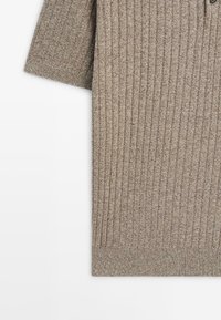 Beige ribbed knit sweater with short sleeves and a button detail on upper right side, displayed on white background.