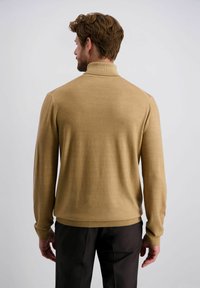Beige gebreide trui met een hoge kraag, lange mouwen en geribde manchetten. Zachte textuur en aansluitende silhouet, gecombineerd met donkere broeken.