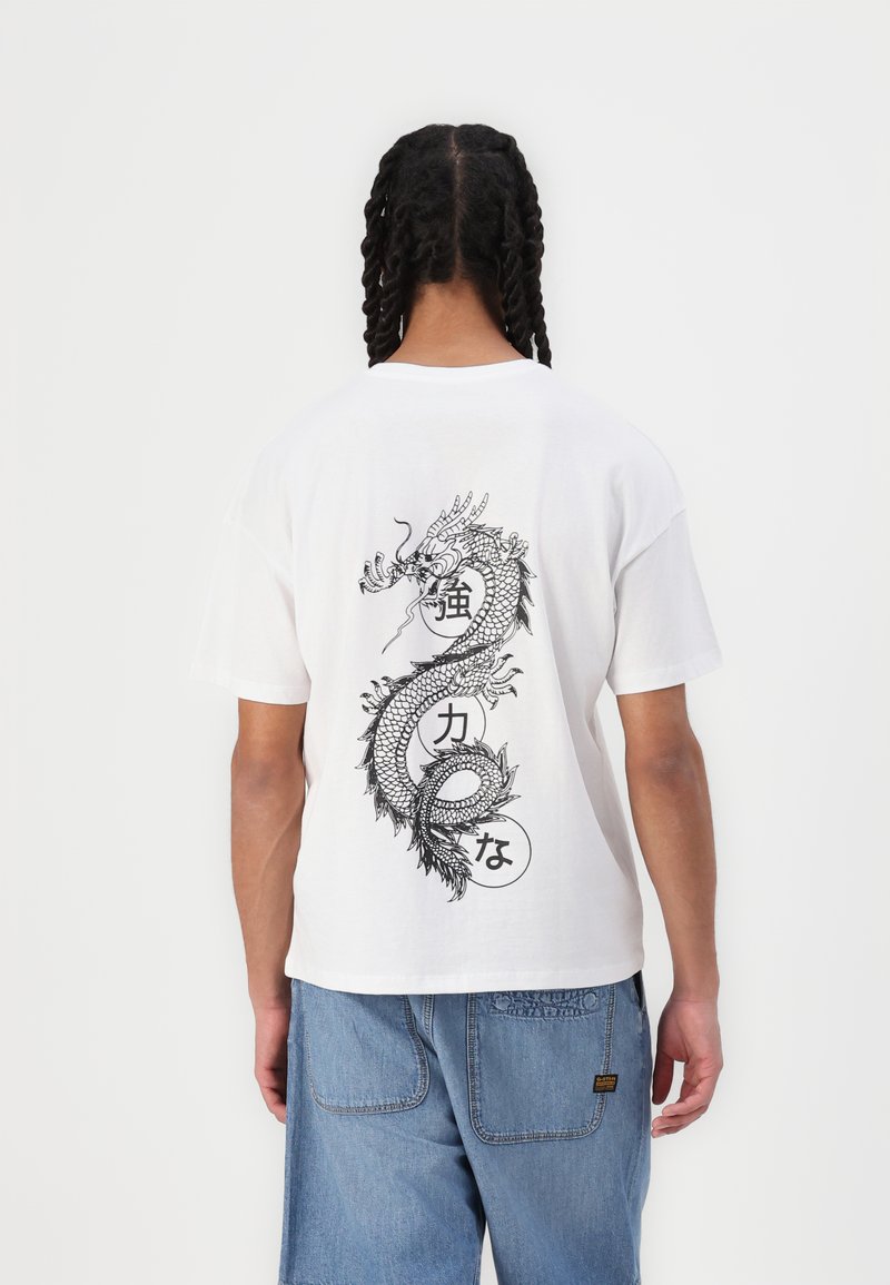 Hvit bomulls t-skjorte med et stort svart dragegrafikk på baksiden, med runde detaljer og japansk tekst integrert i designet.