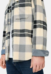 Geruite flanellen shirt in crème, grijs en zwart. Kenmerken zijn knoopsluiting, borstzak en blauwe corduroy mouwen. Zachte textuur, relaxed fit.