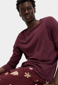 Camisa de manga larga color burdeos combinada con pantalones color burdeos que presentan patrones de hombre de jengibre dorado y estrellas. Tela suave y cómoda con un ajuste casual.