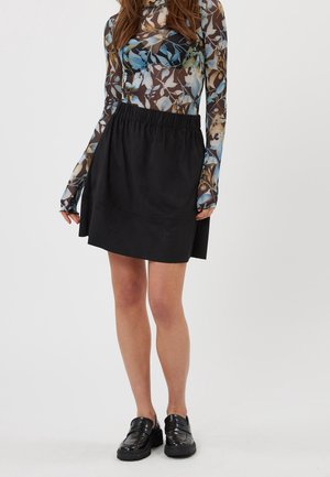Jupe noire en forme A avec une taille élastique. Portée avec un haut en maille à manches longues, orné de motifs floraux dans des tonalités de bleu et de beige.