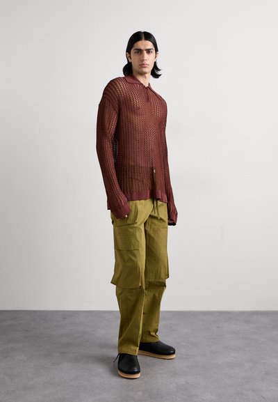 Maglietta a maniche lunghe rossa in rete con colletto, abbinata a pantaloni cargo verdi oliva e zoccoli neri con suola in legno. Design semplice e strutturato.