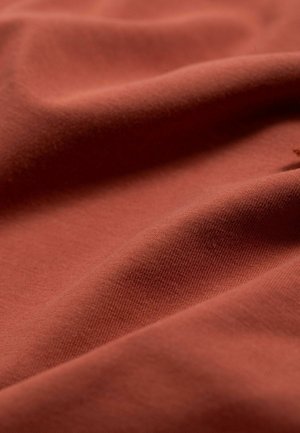 Roestkleurige stof met een gladde, zachte textuur, met subtiele ribbels en zachte plooien. Het materiaal lijkt lichtgewicht en flexibel te zijn.
