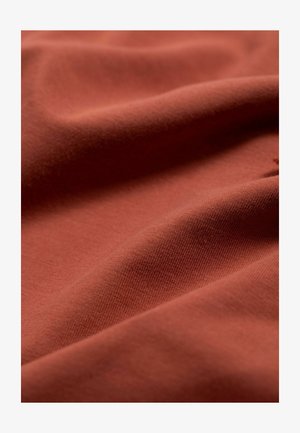 Rostfarbener Stoff mit einer glatten, weichen Textur, der subtile Rippungen und sanfte Falten aufweist. Das Material wirkt leicht und flexibel.