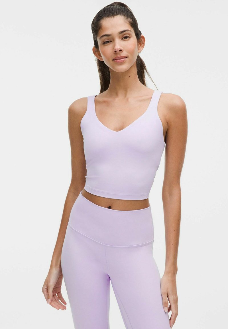Lila sport crop top met brede bandjes en een V-hals, gecombineerd met hoge taille lila leggings. Het materiaal lijkt glad en rekbaar.