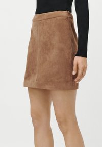 Fustă mini din suede maro, cu un design ajustat, cusături frontale și o închidere cu fermoar discret la spate, care subliniază o textură uniformă.