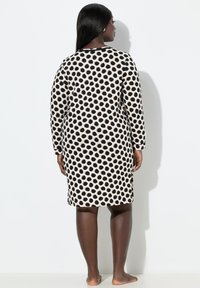 Jurk met lange mouwen, beige basis met grote zwarte polkadots. Zachte stof, knie-lengte ontwerp, ronde halslijn, zonder zichtbare sluitingen.