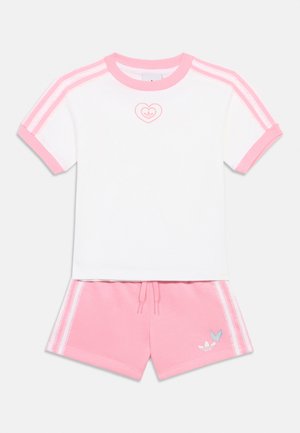 Wit T-shirt met korte mouwen, roze kraag en strepen, gecombineerd met roze korte broek met witte strepen en een vlinderlogo op het been.