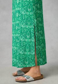 Grön blommig maxi-klänning med sidöppning, gjord av lättviktsmaterial. Kombinerad med grå sandaler med spänne och korksula.