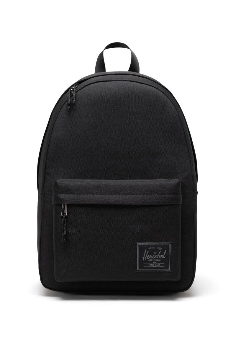 Sac à dos en tissu noir avec une forme arrondie, poche avant, fermetures éclair et une étiquette de logo. Matériau durable et design minimaliste.