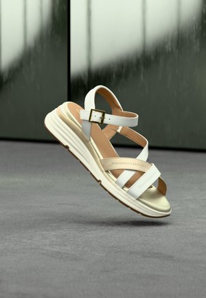 Sandale à brides blanches et beiges avec une semelle rembourrée, une boucle réglable et une semelle intérieure texturée, dotée d'une semelle extérieure en caoutchouc antidérapante.
