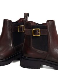 Brown leather ankle boots with elastic side panels and gold buckle accents. Textured finish and rubber soles. Modern chelsea design.