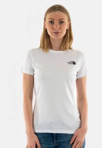 Hvit T-skjorte med korte ermer laget av bomull, med en liten svart logo på venstre bryst. Enkel design med rund hals.