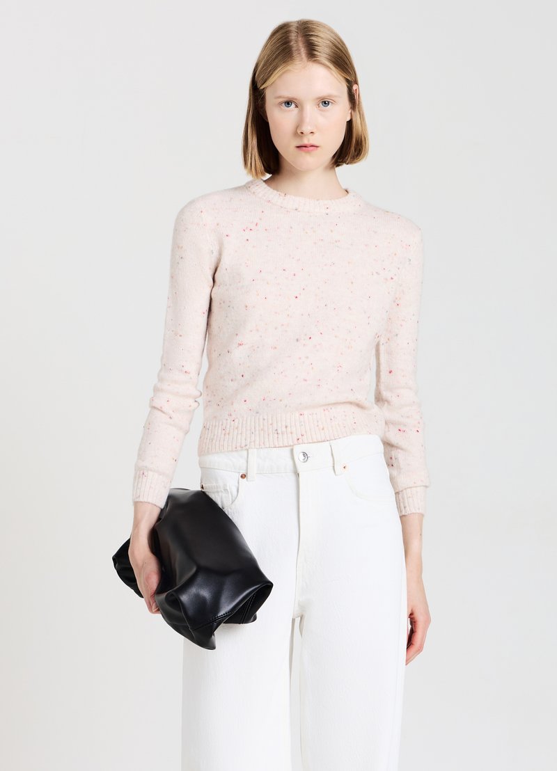 Helles rosa gestricktes Sweatshirt mit gefleckter Textur, Rundhalsausschnitt und gerippten Bündchen, kombiniert mit weißen weiten Hosen und einer schwarzen Clutch.