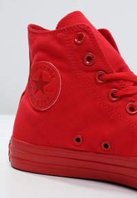 Sneaker alta rossa in tela Converse All Star con lacci rossi e suola in gomma coordinata, mostrata da un angolo laterale e posteriore.