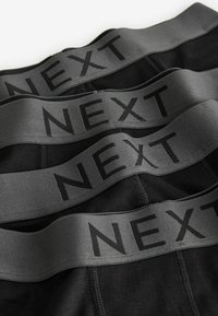 Black boxer briefs with a wide gray waistband featuring the word "NEXT" in black lettering, stacked neatly for display.