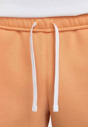 I pantaloni della tuta arancioni presentano una texture morbida, una vita elastica con lacci bianchi e cuciture rinforzate per garantirne la durata.