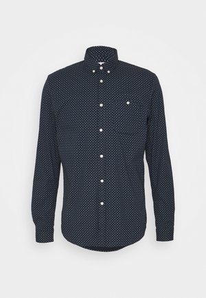 Chemise à manches longues bleu marine avec un motif géométrique blanc, dotée d'un col classique, d'une poche avant et d'un ourlet arrondi.