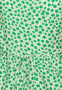 Robe à imprimé floral vert avec de petites fleurs sur un fond clair, taille cintrée et détail noué à l'avant.