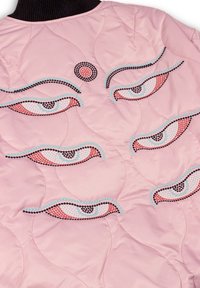Roze gewatteerde jas met ingewikkelde geborduurde oogmotieven in zwart, blauw en roze, voorzien van een geribbelde zwarte kraag en golvende stikpatronen.