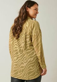 Lightweight, olive green blouse featuring a wavy pattern and transparent texture. Long sleeves with buttoned cuffs and a curved hemline.