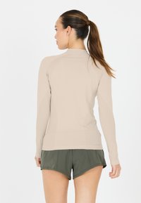 Langærmet ribbet top i beige med høj hals og tætsiddende design. Kombinationen med grønne sports-shorts fremhæver et sporty look.