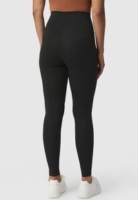 Zwarte high-waisted leggings van rekbaar materiaal, met een gladde textuur en een strakke pasvorm, gecombineerd met witte sneakers.
